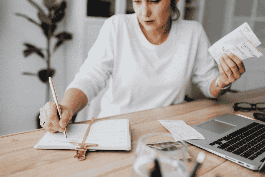 Femme à son bureau avec ordinateur portable, reçus et carnet pour suivre ses dépenses et gérer son budget grâce à l’open banking au quotidien