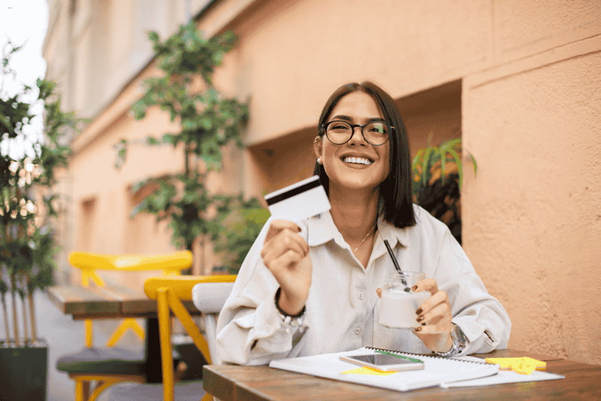 Jeune femme souriante tenant une carte bancaire blanche dans un café.