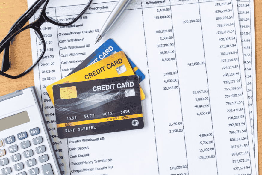 Trois cartes de crédit posées sur un relevé bancaire avec une calculatrice et des lunettes.