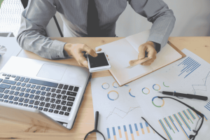 Homme en chemise analysant des graphiques financiers avec un ordinateur portable et un smartphone, dans un contexte de planification de crédit.