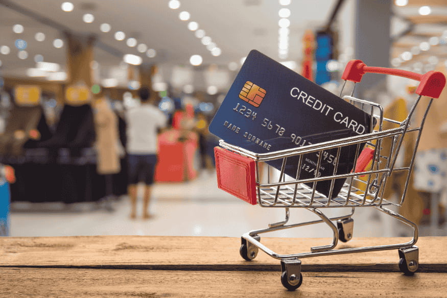 Carte de crédit insérée dans un chariot de supermarché miniature, en magasin.