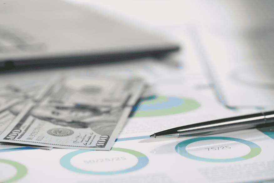 Billets de 100 dollars américains posés sur des graphiques financiers colorés avec un stylo.