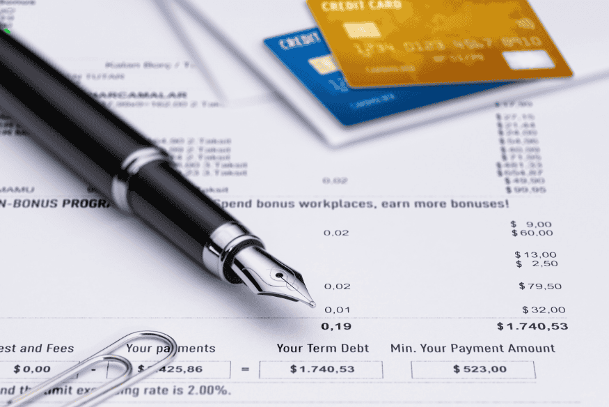Stylo-plume posé sur un relevé de carte de crédit avec deux cartes bancaires visibles en arrière-plan.