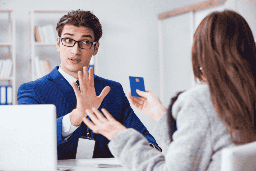 Conseiller bancaire refusant une carte à une cliente, illustrant un refus d’ouverture de compte ou de crédit.