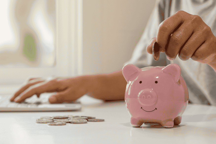 Main déposant une pièce dans une tirelire rose en forme de cochon, représentant l’épargne pour anticiper les dépenses imprévues.