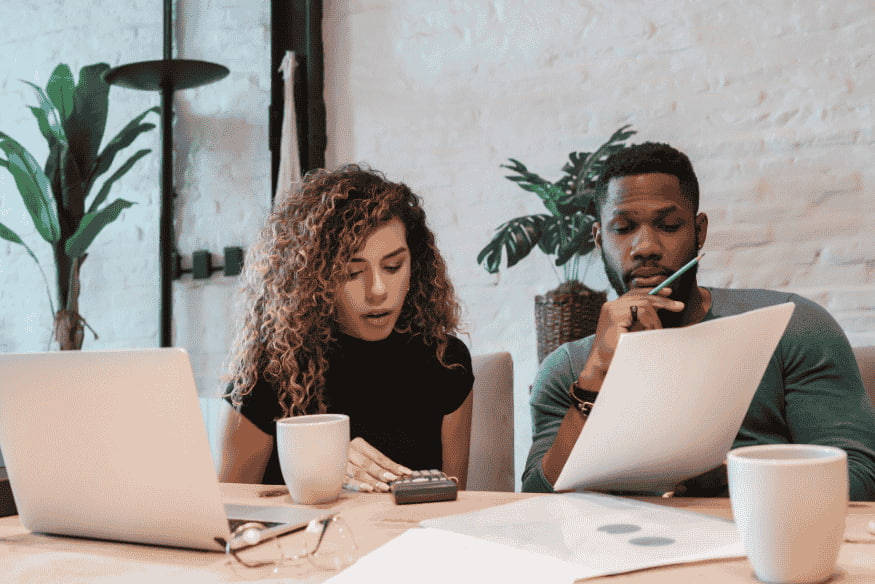 Couple analysant ses dépenses mensuelles avec un ordinateur portable et une calculatrice pour établir un budget efficace en 2025.