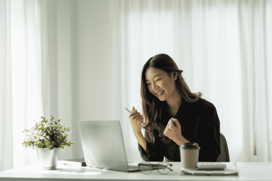 Femme souriante célébrant un succès financier devant un ordinateur portable, illustrant l’importance d’un budget mensuel efficace en 2025.
