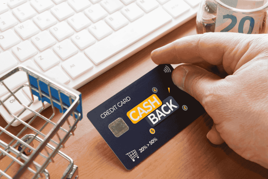 Carte de crédit cashback tenue par une main près d’un clavier et d’un caddie miniature.