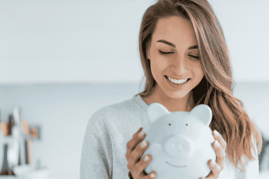 Femme souriante tenant une tirelire bleue, illustrant les économies personnelles et la réussite du défi d’épargner 500 euros par mois.