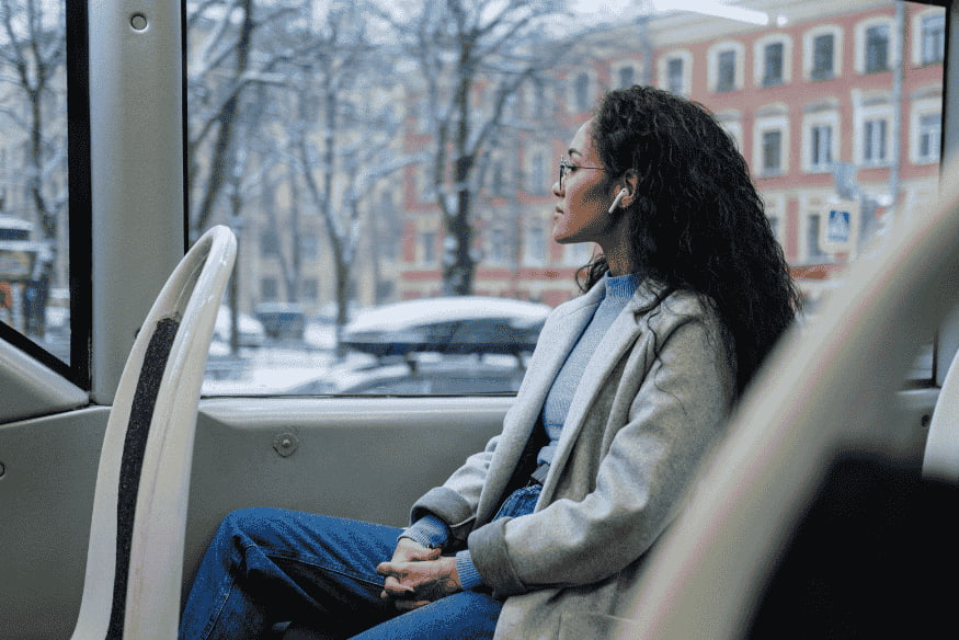 Femme assise dans un bus regardant par la fenêtre en hiver, représentant une alternative économique aux déplacements en voiture.