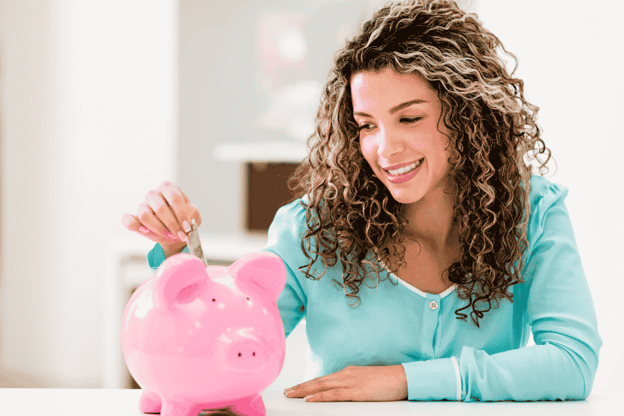 Femme souriante déposant de l’argent dans une tirelire rose, illustrant un défi d’épargne mensuel simple et motivant.