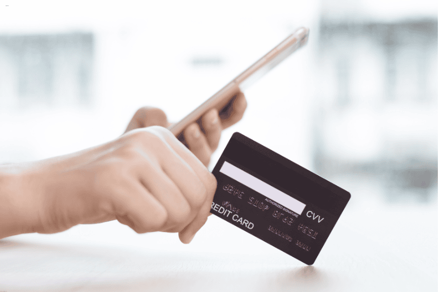 Main tenant une carte de crédit et un téléphone portable, symbolisant une demande de carte bancaire via application mobile.