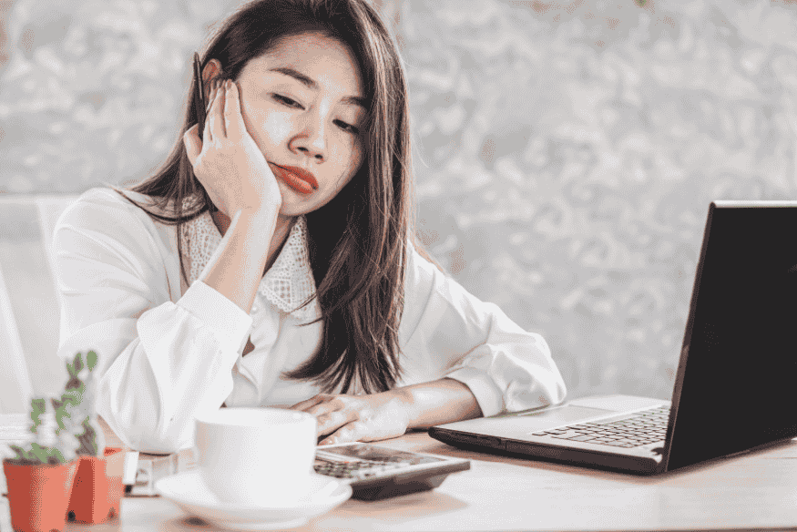 Femme stressée devant un ordinateur, préoccupée par les difficultés d’épargner sur le long terme pour un projet personnel.