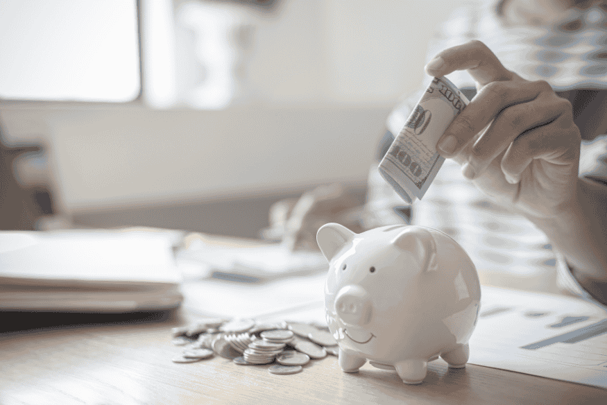 Personne plaçant un billet dans une tirelire pour créer une habitude d’épargne durable et atteindre ses objectifs financiers.