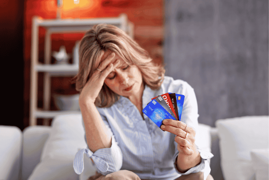 Femme inquiète tenant plusieurs cartes bancaires, victime de frais multiples ou non identifiés.