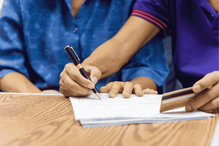 Main signant un contrat tandis qu’une autre tient une carte bancaire, illustrant des conditions souvent négligées.