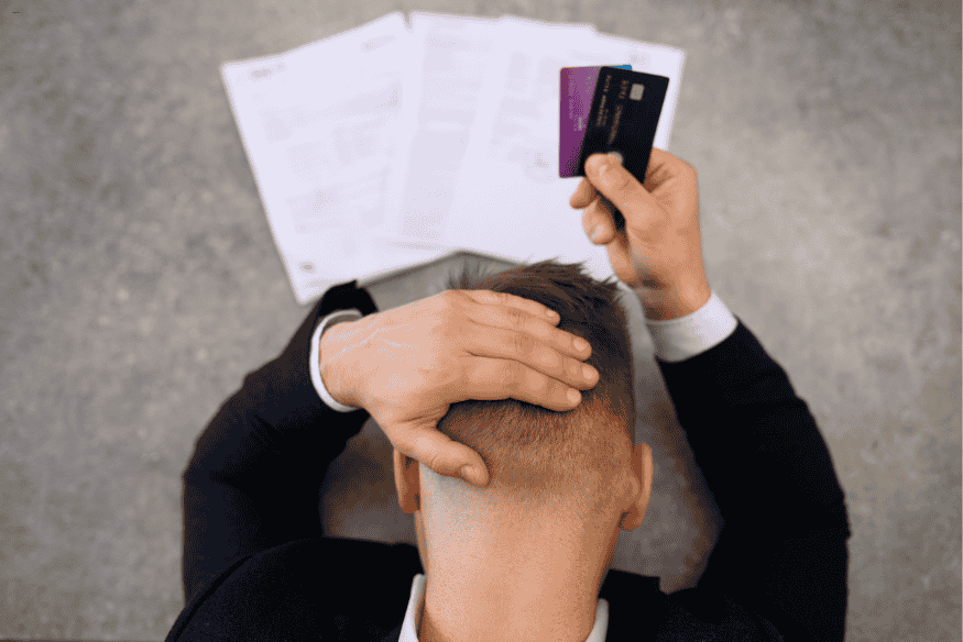 Homme assis, stressé en tenant des cartes bancaires face à des factures impayées.