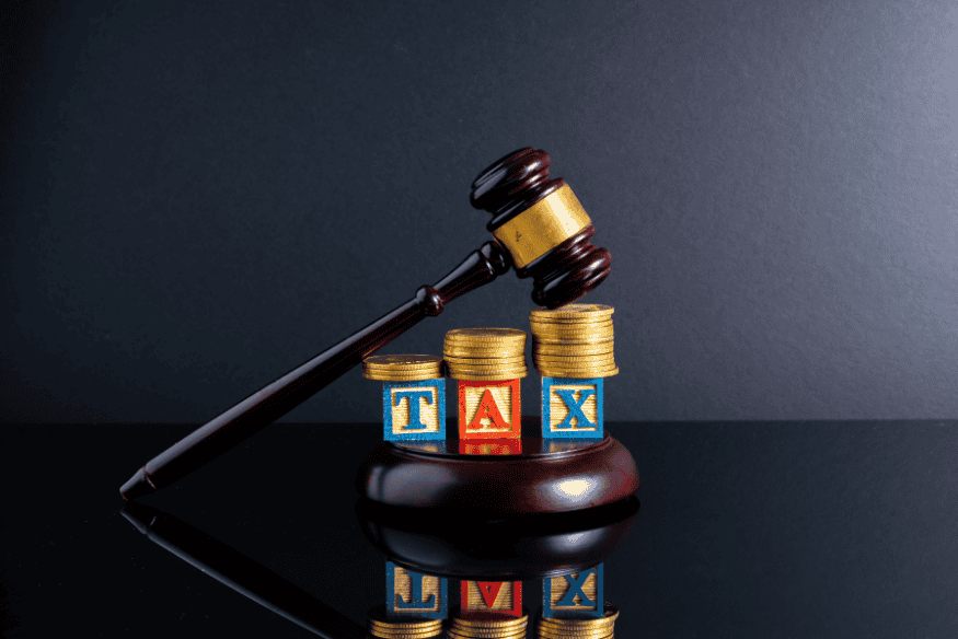 Marteau de justice posé sur des pièces et blocs formant le mot "TAX", symbolisant la fiscalité liée aux revenus irréguliers en France.