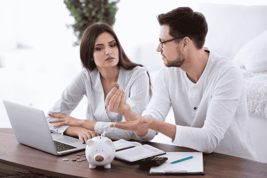 Couple discutant de finances domestiques avec un ordinateur portable, un carnet et une tirelire, symbolisant les bases d’un budget partagé à deux.
