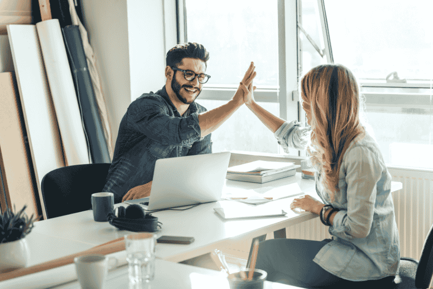 Deux collègues se félicitent avec un high five dans un bureau, symbolisant la réussite grâce à de bonnes habitudes financières à long terme.