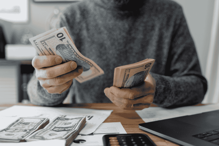 Personne comptant des billets de banque sur une table, symbolisant la gestion financière personnelle et la réflexion sur la valeur de l'argent.