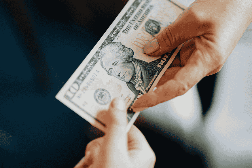 Échange d’un billet de dix dollars entre deux mains, illustrant une transaction financière entre particuliers.
