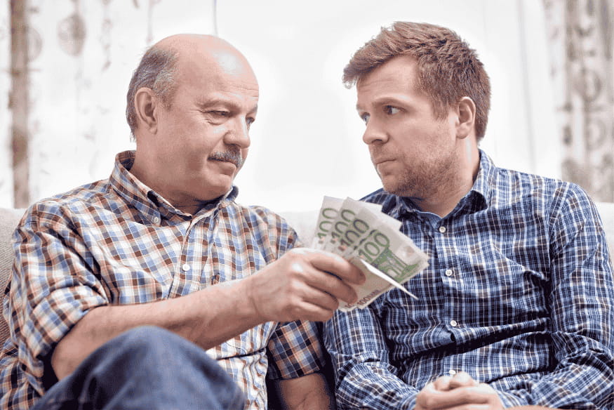 Un homme plus âgé prête de l’argent en espèces à un homme plus jeune, illustrant un prêt entre particuliers dans un cadre familial.