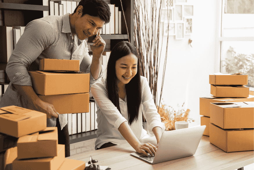 Auto-entrepreneurs gérant une activité e-commerce, entourés de colis, illustrant le succès d’un projet financé par un prêt adapté.