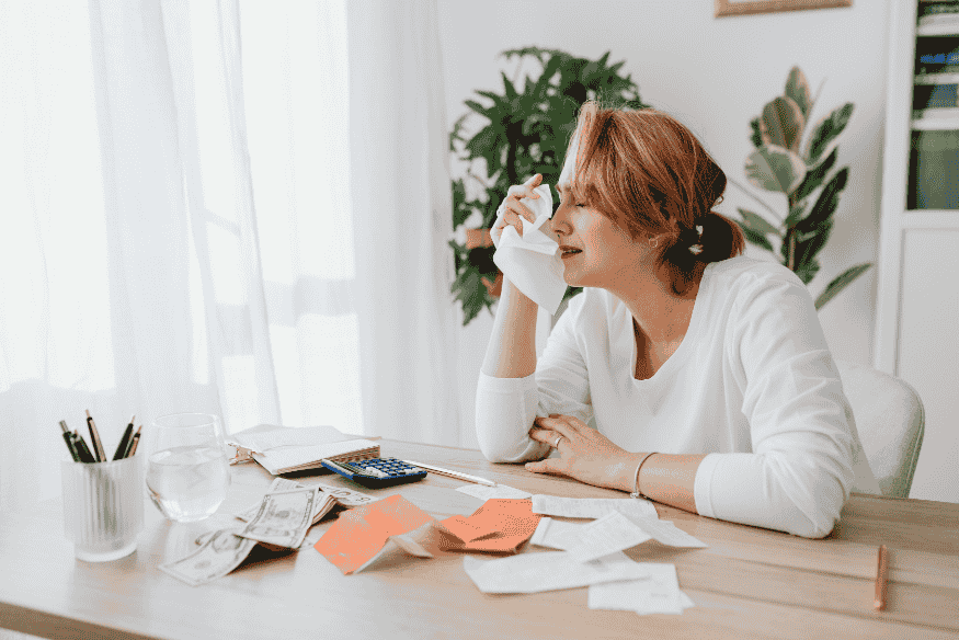 Femme stressée par ses finances, assise à une table avec des factures, de l'argent liquide et une calculatrice.