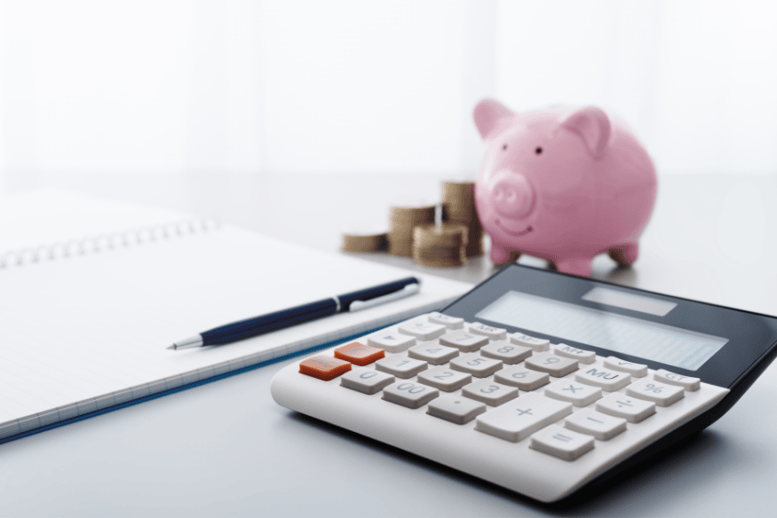 Calculatrice, tirelire rose et pièces de monnaie sur un bureau, symbolisant une gestion consciente et équilibrée de ses finances personnelles.