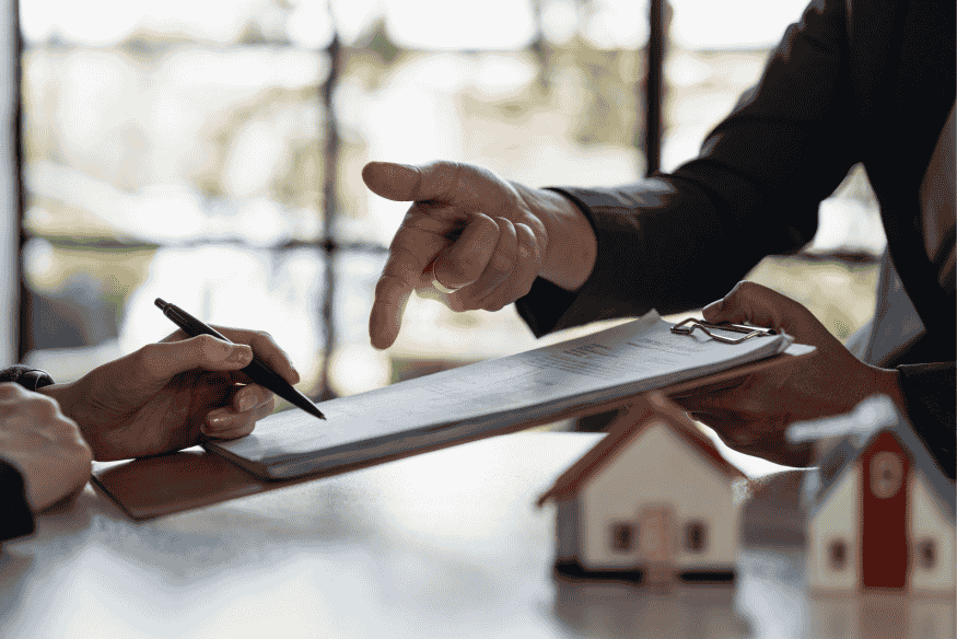 Discussion entre deux personnes autour d’un contrat de rachat de crédit immobilier, avec maquettes de maisons sur la table.