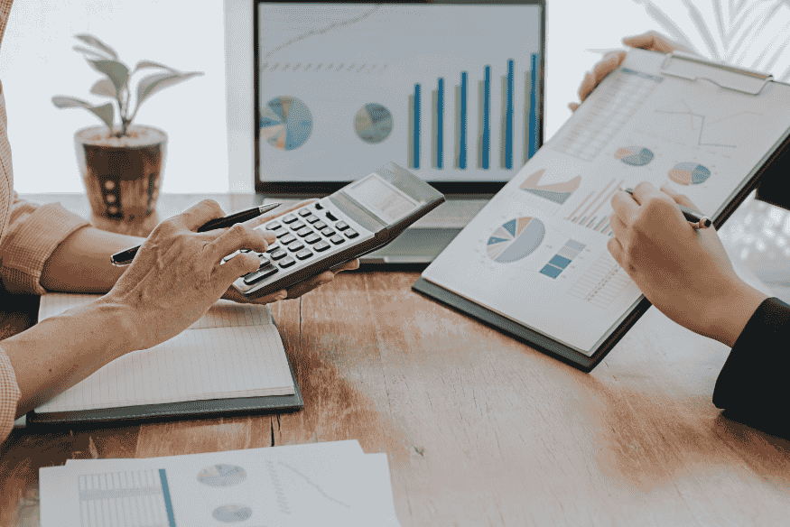 Deux personnes analysent des graphiques financiers avec une calculatrice, illustrant l’importance d’une routine financière hebdomadaire pour une meilleure gestion de budget.