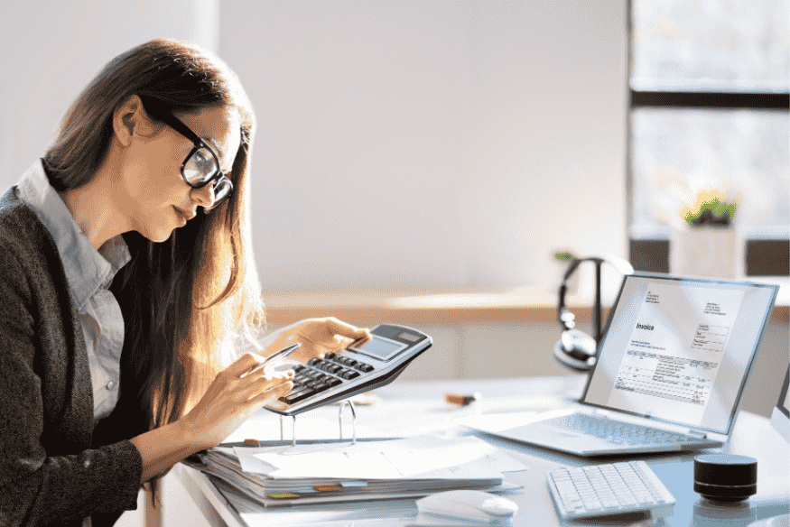 Femme utilisant une calculatrice devant son ordinateur pour vérifier ses comptes bancaires et paiements automatiques dans le cadre d'une routine financière.