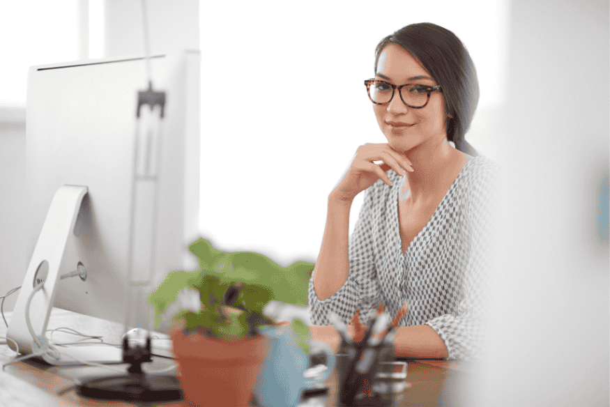 Femme souriante assise à son bureau, illustrant la sérénité obtenue grâce à une routine financière hebdomadaire efficace.