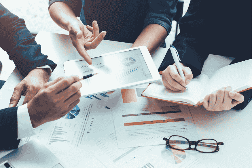 Réunion d’experts analysant les résultats de simulations de prêt sur une tablette et des documents financiers imprimés.