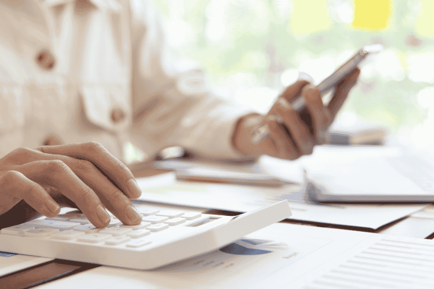 Personne utilisant une calculatrice et un smartphone pour planifier ses dépenses importantes, illustrant une gestion budgétaire moderne.